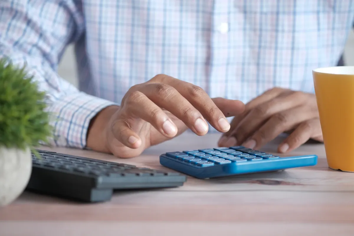 A person using a calculator at a desk, planning the cost of a web accessibility project.